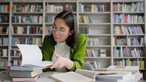 Asian Female Student Makes Summary in Notebook in Library