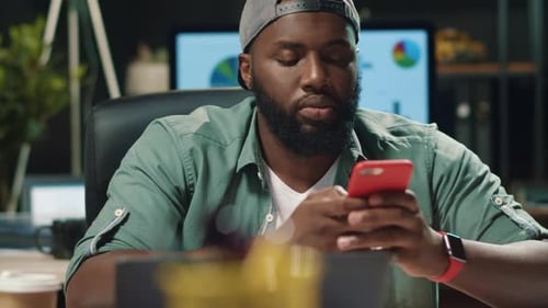 Young african american man types message on mobile phone in modern office