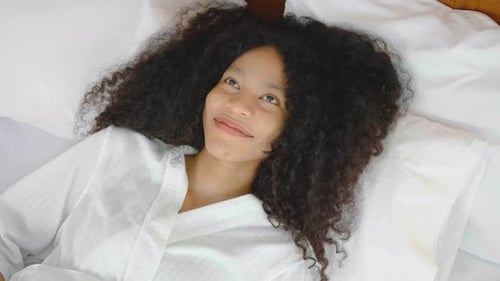 Happy young African American woman falls on the bed in room. Beautiful girl smiling