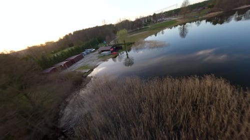 FPV drone shot flying over reeds and a mirroring lake surface on a spring day