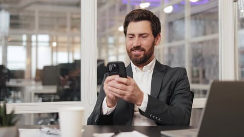 Businessman Sitting at Desk and Typing on Phone in Modern Office