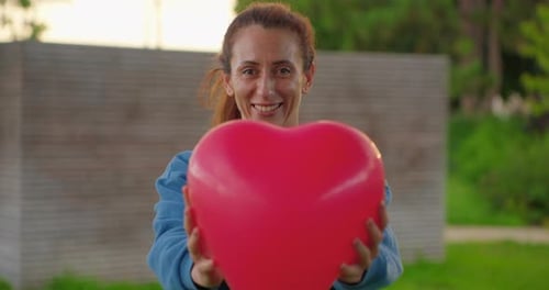 Woman Holding Heart Balloon Smiling Outdoors