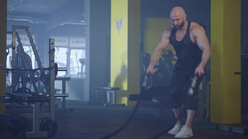 The Athlete Trains in the Hall and Performs Workout Exercises with Battle Ropes