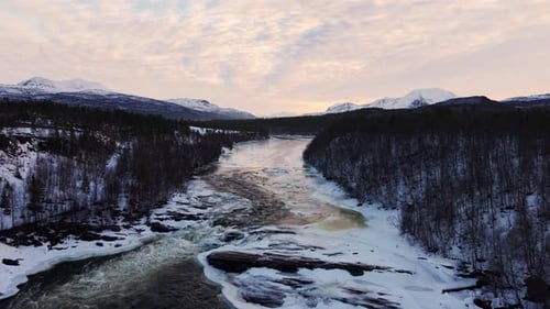 Luftaufnahme eines wilden Flusses, der durch eine verschneite norwegische Berglandschaft fließt