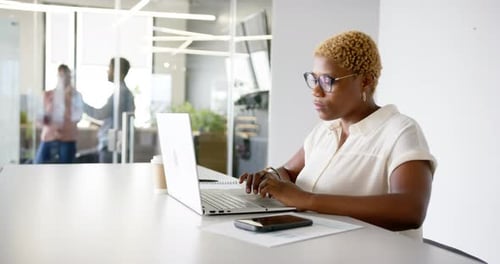 Working at desk, woman using laptop and smartphone in modern office
