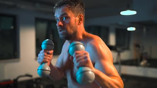 Boxer Practices Punches with Dumbbells in His Hands in the Gym in the Evening