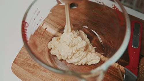 Squeezing mayonnaise into glass measure bowl.