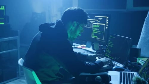 A Cybersecurity Expert is Working Hard in a Dimly Lit Environment with Multiple Screens
