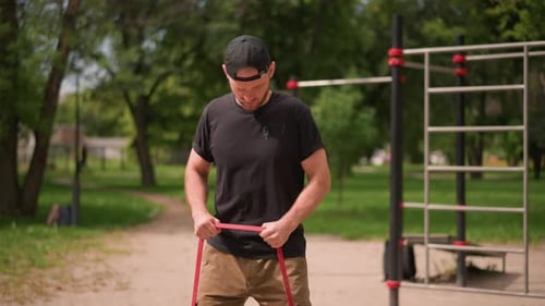 White Athlete In Park Inspecting Resistance Band And Adjusting Grip For Workout Attentive Movements
