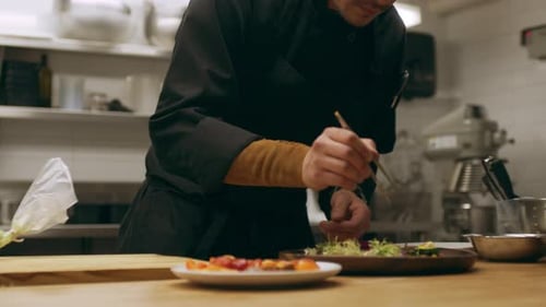 Professional chef carefully garnishing salad in restaurant kitchen