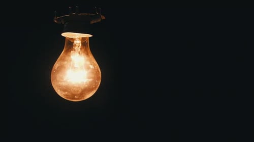 Die Glühlampe am Kabel wird ein- und ausgeschaltet und flackert auf schwarzem Hintergrund