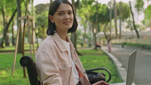 Portrait of Young Cheerful Woman with Laptop in Park