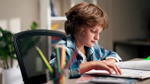 Close Up in the Children's Room a Schoolboy in a White Sweater and a Blue Checkered Shirt at a Desk
