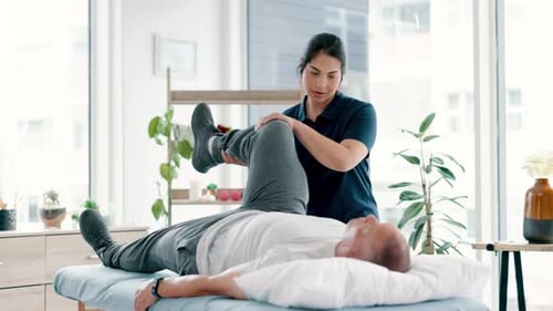 Physical Therapist Assists Senior Man with Leg Exercises