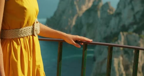 Woman resting her hand on a balcony rail while admiring Capri cliffs and open sea view