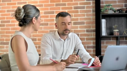 A woman and a man working and talking in the office. Gadgets and papers with information
