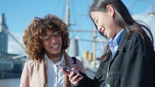 Cheerful Female Colleagues Using Smartphone and Chatting Outdoors in the City
