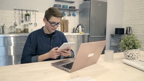 Teenager uses tablet and laptop in kitchen