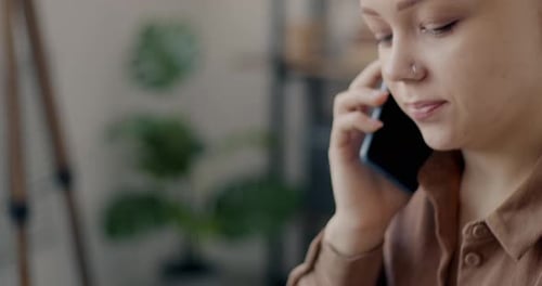 Closeup of Young Businesswoman Speaking on Cellphone and Typing with Laptop in Office