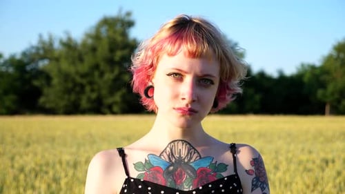 Portrait of Unhappy Punk Girl with Ear Tunnels with Blurred Wheat Green Field at Background Serious