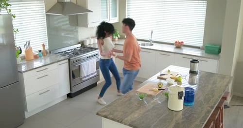 Asian man reaching for woman's hand, playful dancing with African American woman in kitchen avocado