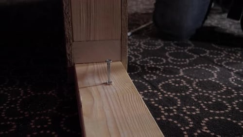 close-up of a piece of wood with a man's hand driving a nail into the wood with a hammer