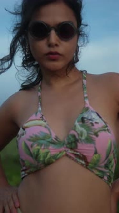 Woman in floral bikini with sunglasses poses confidently outdoors with wind in her hair