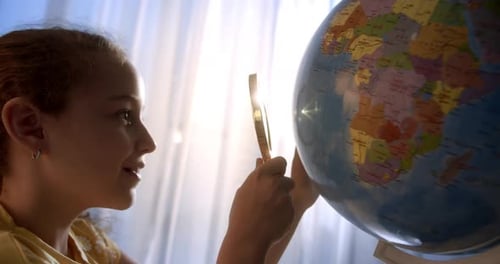 Girl Examining Globe with Magnifying Glass Indoors