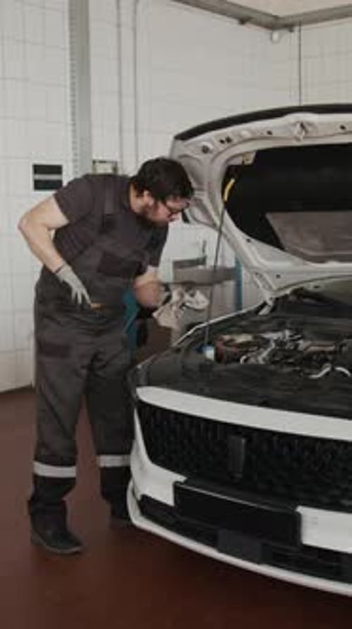 Vertical of Mechanic Checking Engine Oil Level with Dipstick in Garage