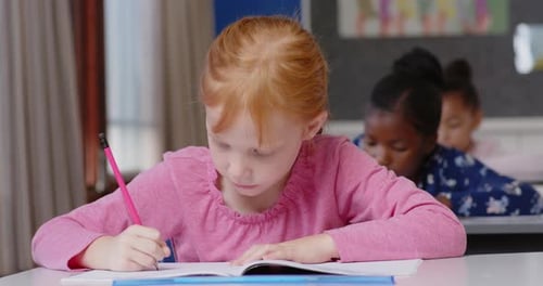 In school, girl writing in notebook while classmate looks on in classroom