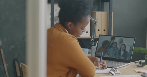 Young Woman Talking to Group of Female Colleagues During Online Video Call Using Laptop in Office