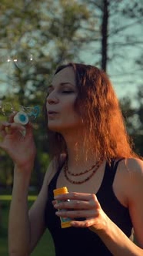 Vertical of Female Making Soap Bubbles Beautiful Tree with Orange Leaves