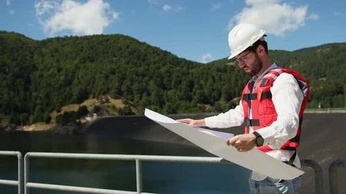 Engineer with White Helmet Holds a Project of the New Dam