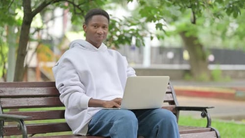 Casual African American Man Smiling with Laptop in Park