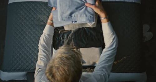 Mature Businessman Folding Clothes and Packing Luggage in Bright Hotel Room Before Departure