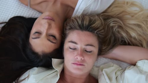Top View of Two Beautiful Women in Bed Who Sleep with Their Heads Leaning Against Each Other
