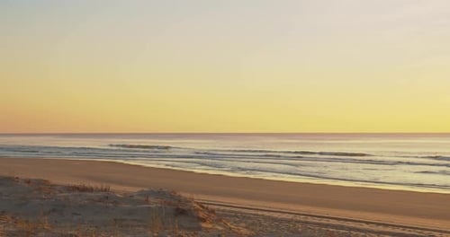 View of the waves and beach from sand dune during colorful yellow tones sunset