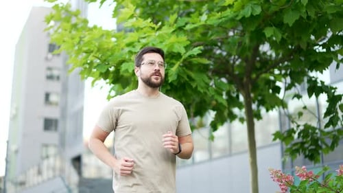 Adult male runner jogging in urban city street. Handsome active man with headphones enjoys jogging