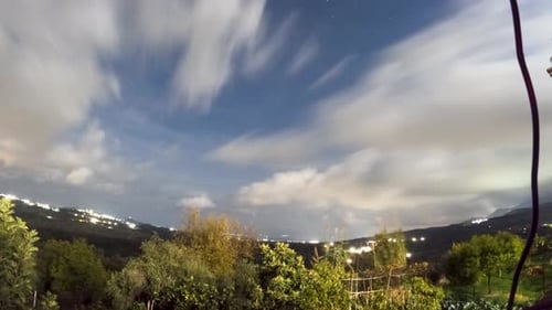 Night Sky Time Lapse with Fast Moving Clouds and Stars Over Rural Landscape and City Glow