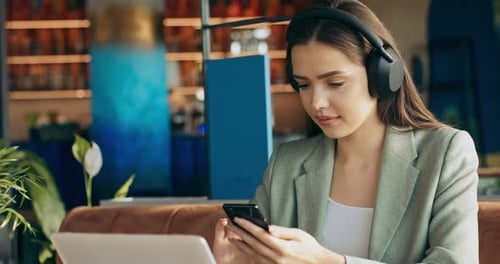 Beautiful Adorable Young Woman in Wireless Headphones Wearing Buisness Suit Sitting at Restaurant