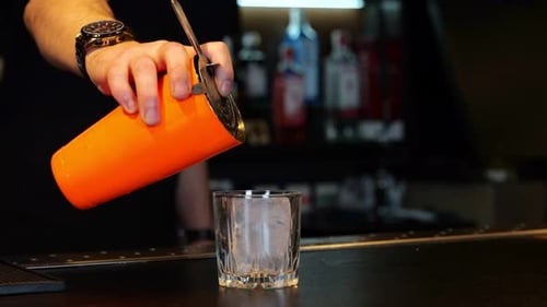 Barman Pouring Fresh Alcoholic Drink Into the Glasses with Ice Cube on the Bar Counter Cropped Real
