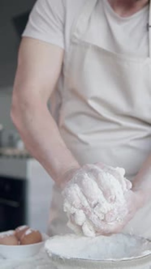 Ein Koch knetet den Teig mit den Händen und beginnt, Brot und Nudeln zuzubereiten. Vertikaler Schuss.