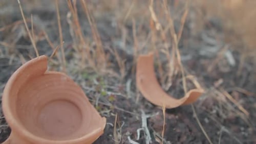 Brown clay pot on the ground broken in half near a white and yellow bowel with white glue