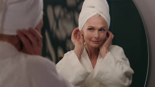 Mature Woman Looks in Mirror, Applies Face Cream