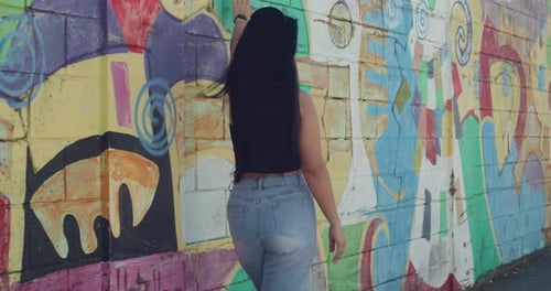 A girl in urban street style is walking in the city, with graffiti art as her backdrop.