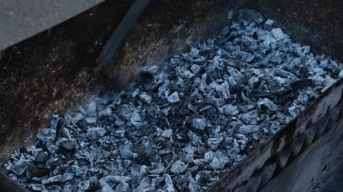 Stirring Embers in a Metal Barbecue Pit