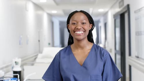 Portrait of happy african american female doctor wearing scrubs in hospital, slow motion