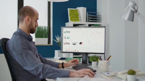 Man Working at Desk with Computer Displaying Data