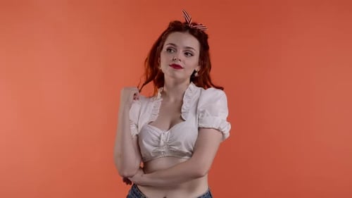 In the Frame on Red Background Young Redhaired Woman with Bright Makeup She Looks Away Twirling a