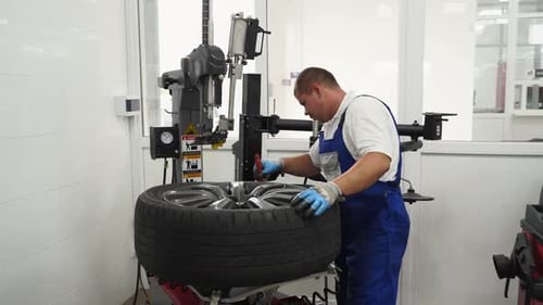 Auto Mechanic Operates Tire Changer Machine at Garage Professional Mounts Car Wheel Seasonal Tire